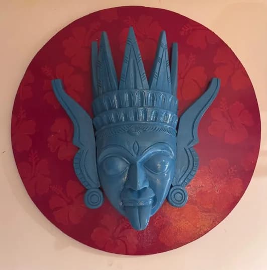 Hand-carved blue wooden mask mounted on a hand-painted red disc